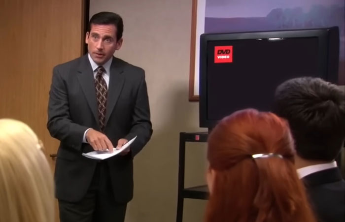 Man in a business suit presenting wild things people say they’ve seen to an attentive audience in an office setting