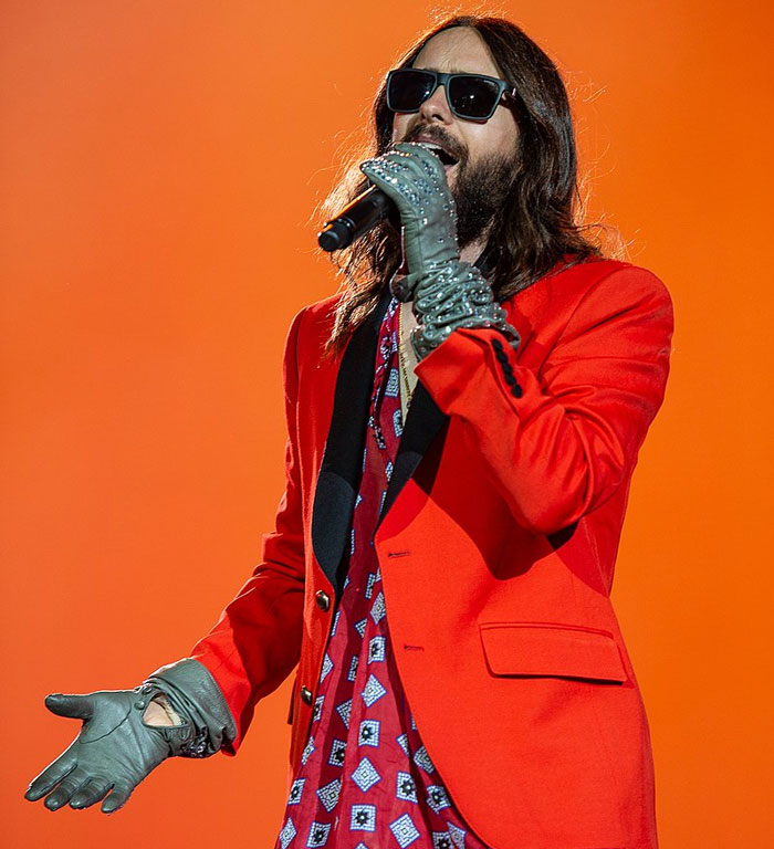 Male singer wearing sunglasses and red jacket performing on stage, related to famous people who did evil things.
