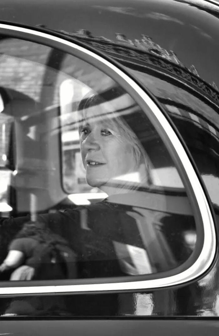 Black and white street shot of a woman inside a car capturing the poetry of everyday life through photography.