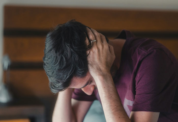 Man in a maroon shirt holding his head in distress, depicting intense emotions during therapy revelations.