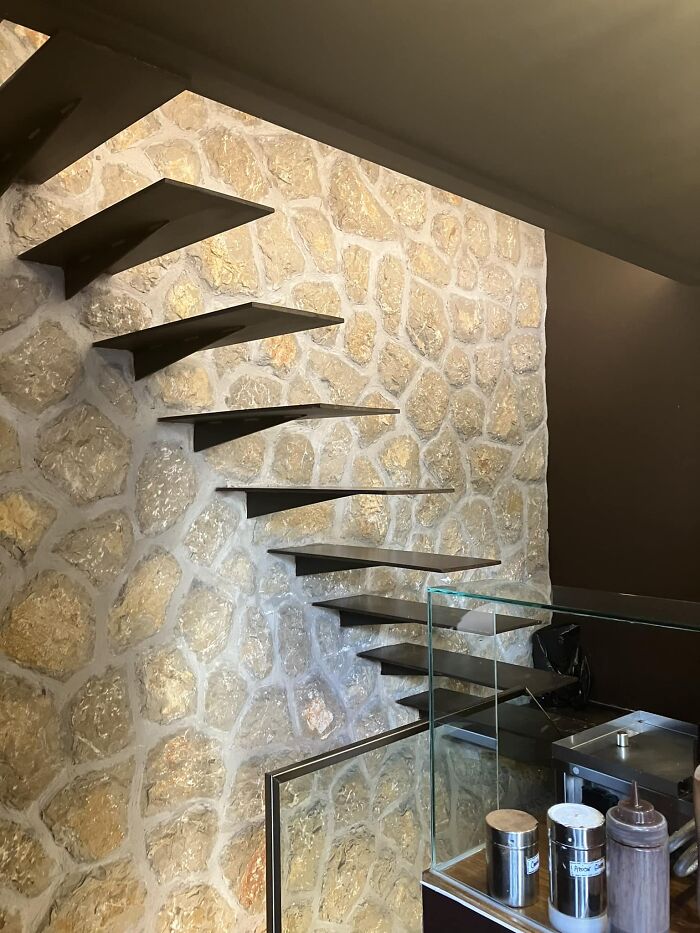 Floating metal stairs attached to a stone wall with no railing, a risky example of death stairs in modern design.
