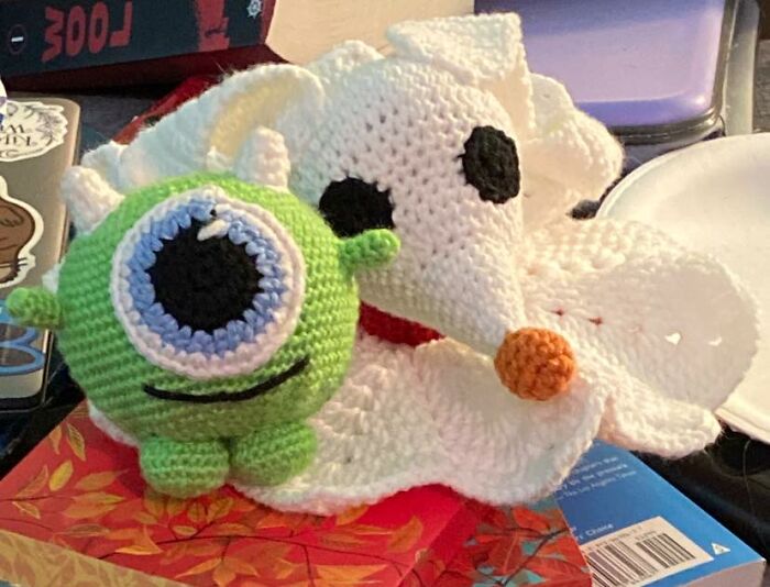 Crocheted amigurumi figures of a green cyclops and a white mouse displayed on a colorful surface in a cozy setting.