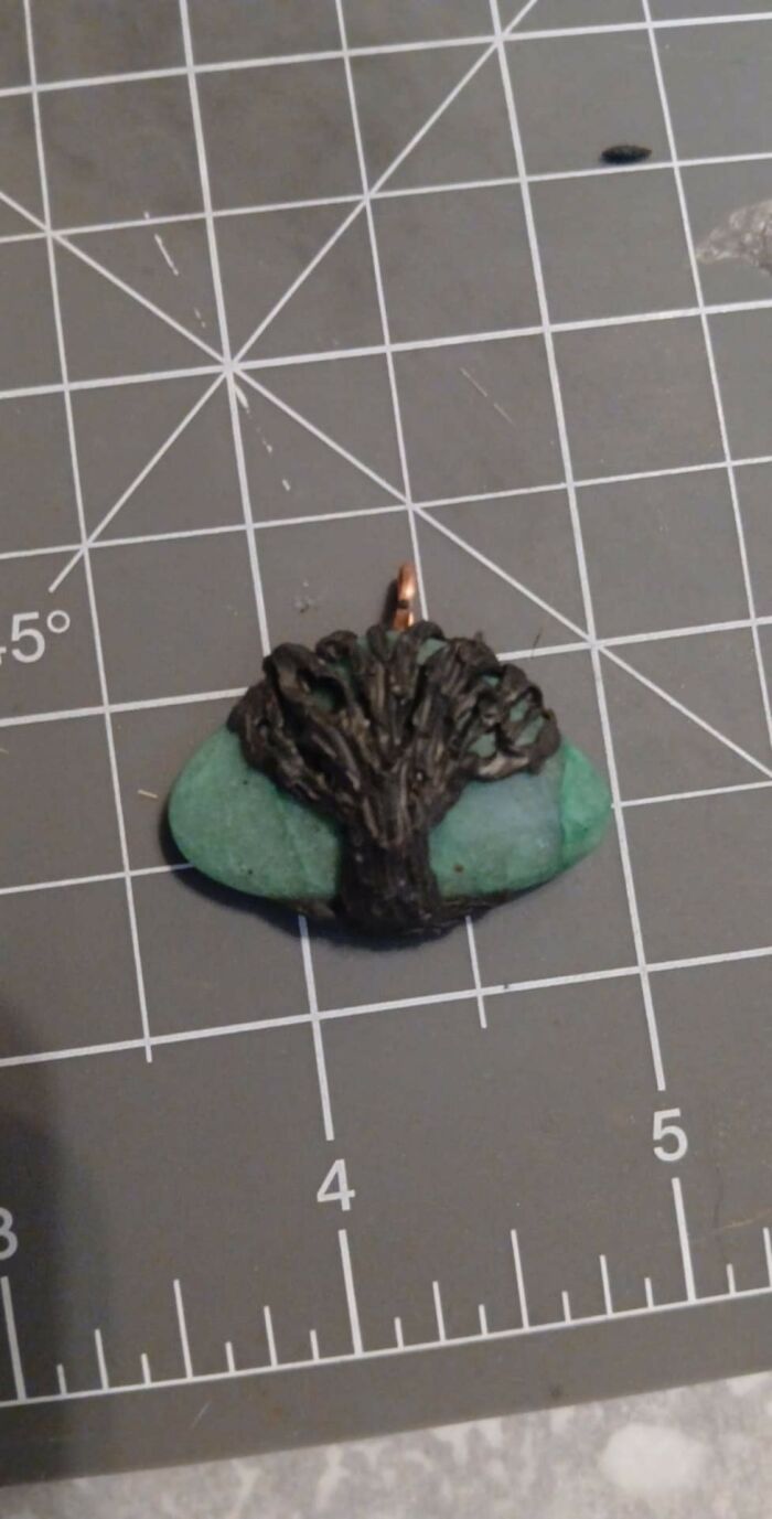 Small handmade pendant with a tree design on a green stone, displayed on a craft cutting mat, DIY project craft shaming.