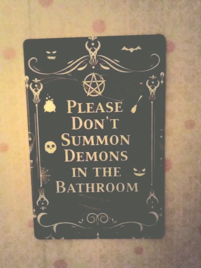 Funny sign warning not to summon demons in the bathroom, adding chaos with humorous decor and spooky design elements.