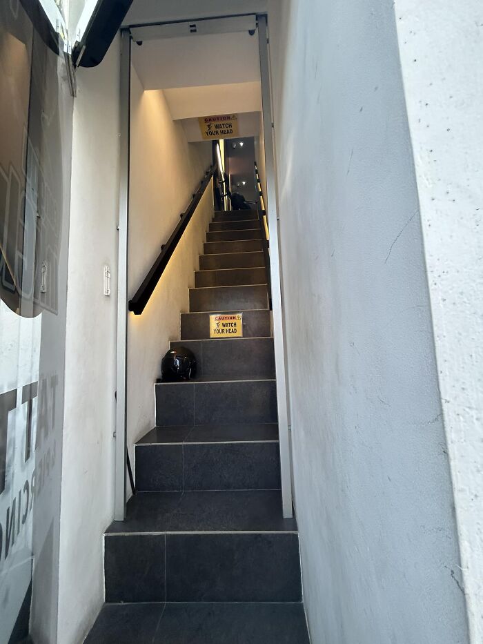 Narrow, steep death stairs with warning signs to watch your head and a helmet placed on one step.