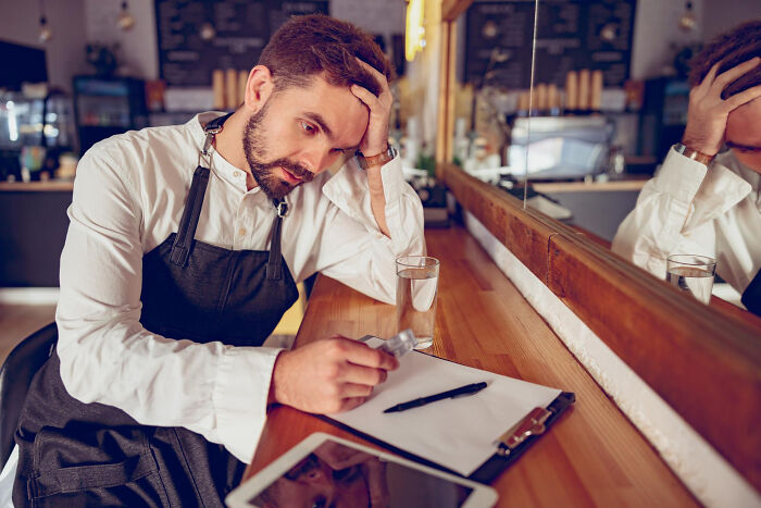 Man in apron sitting at a table, looking stressed and disappointed, reflecting on moments of realizing a friend was a jerk.