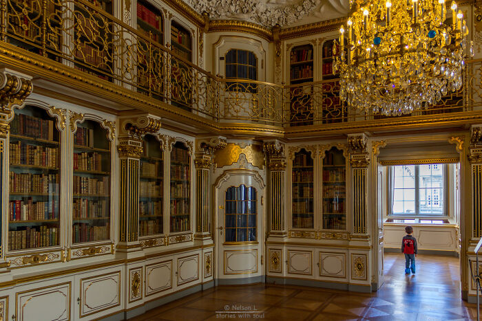 Ornate and stunning historic library interior with gilded details, glass-fronted bookshelves, and a child exploring the space.