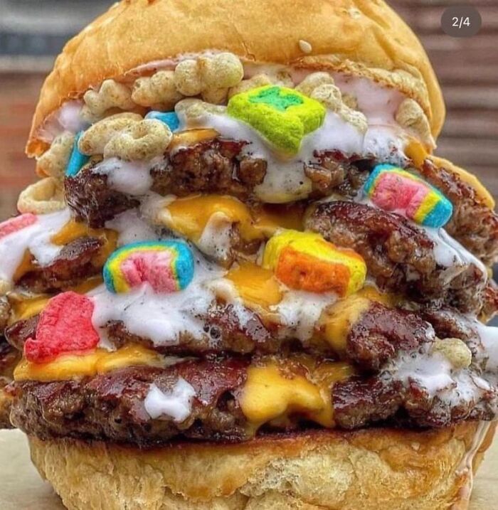 Close-up of a cursed food burger topped with melted cheese, colorful marshmallows, and cereal pieces, creating an unusual mix.