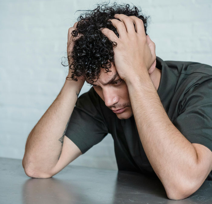Man with curly hair looking stressed and holding head, depicting poor parenting and potential custody issues.