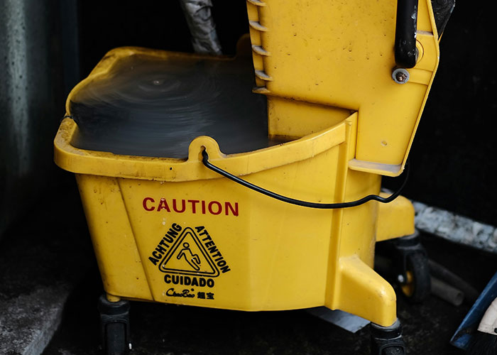 Yellow mop bucket with caution sign filled with water, highlighting a common workplace take one for the team moment.