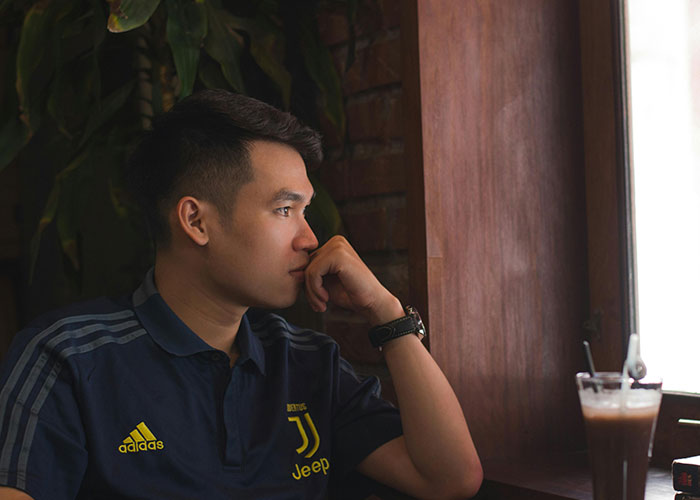 Young man in a Juventus shirt looking thoughtfully out a window during an awkward date at a cafe with a drink nearby.