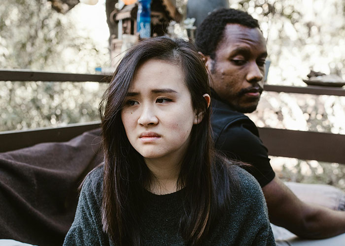 A woman looks upset while a man sits turned away, illustrating emotions related to called off engagements and cheating.