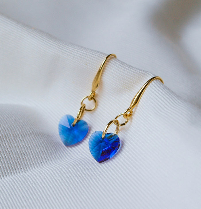 Gold earrings with blue heart-shaped crystals displayed on white textured fabric for how I paid for college tips.