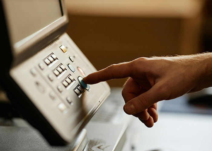 Close-up of hand pressing a button on an obsolete office fax machine still used daily in a vintage setting.