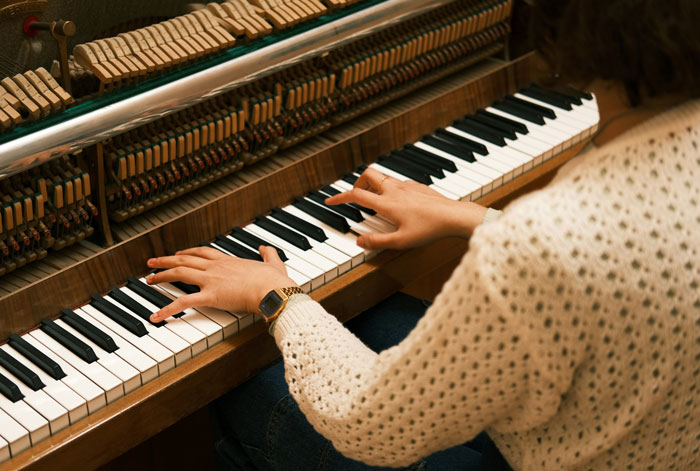 Person in a knit sweater playing an upright piano, illustrating millennials reflecting on biggest lies told growing up.