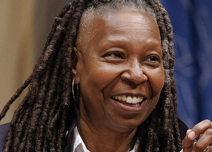 Smiling woman with long dreadlocks and hoop earrings sharing stories about celebrities before fame found them.