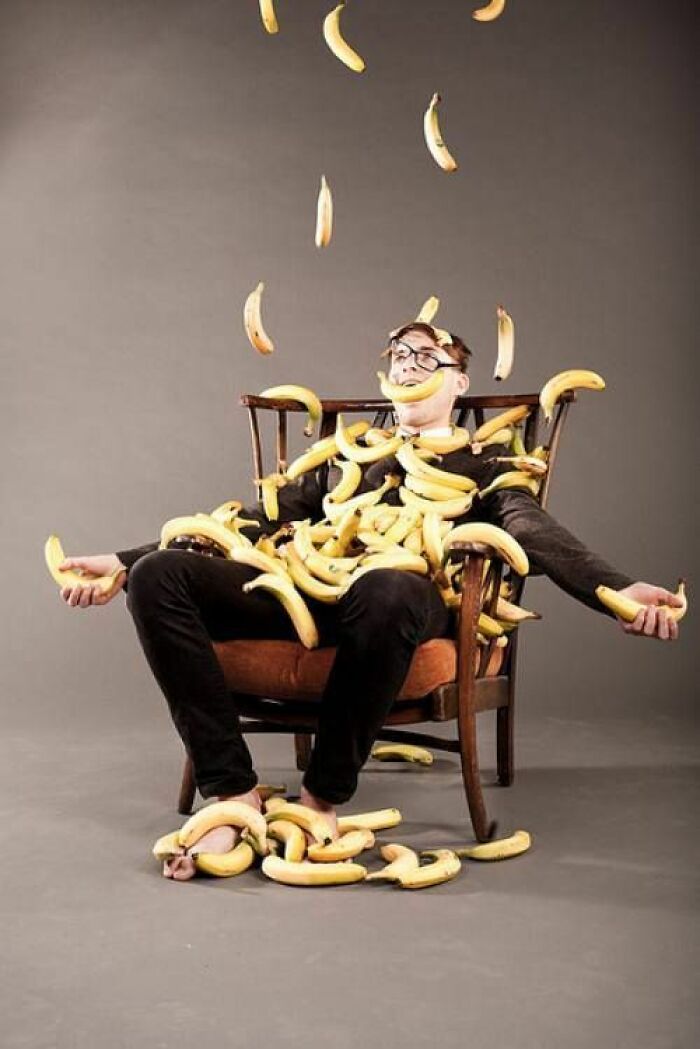 Man sitting in chair covered in falling bananas, a funny meme moment to help forget a hard day.