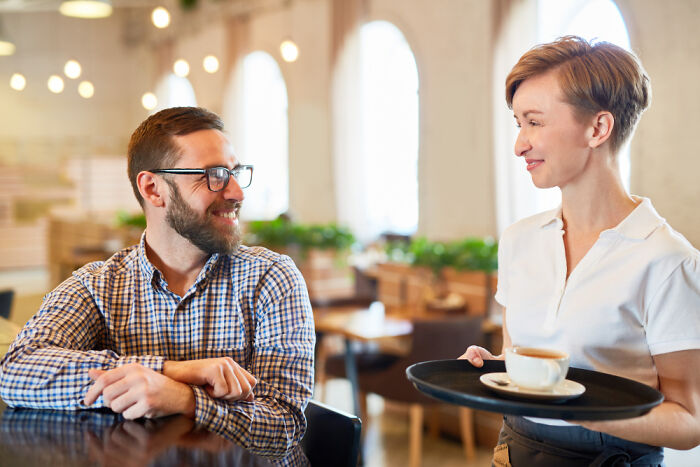 Man smiling and chatting with waitress serving coffee, illustrating golden travel hacks for enjoyable trips.