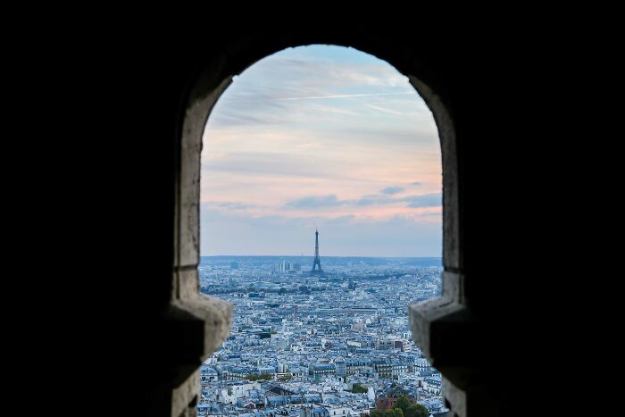 View of the Eiffel Tower and Paris cityscape at sunset framed by a stone arch, a breathtaking travel photo.