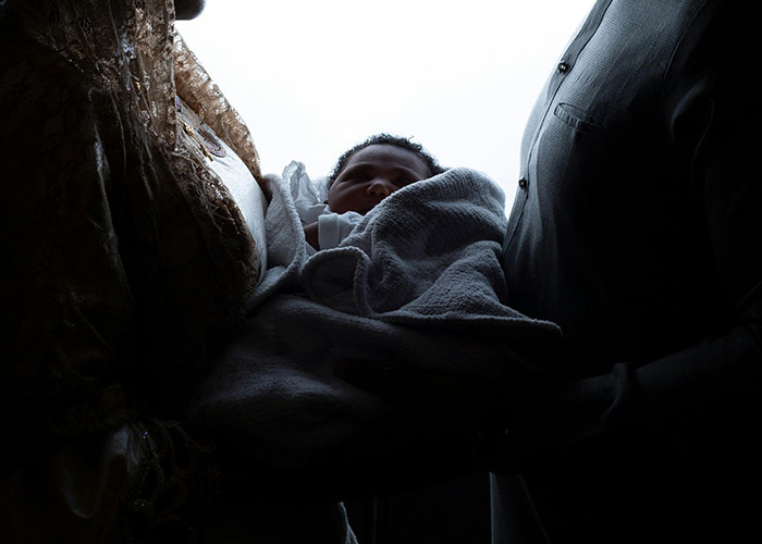 New father holding newborn baby inside dimly lit birthing room, capturing dads' real first-time experiences.