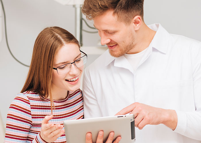 A smiling young woman and man looking at a tablet, illustrating women sharing unhinged things men said about their looks.