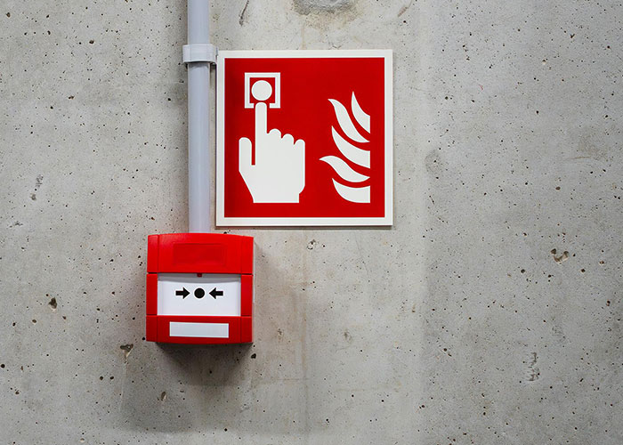 Red fire alarm and emergency button mounted on a concrete wall symbolizing a take one for the team moment in safety.