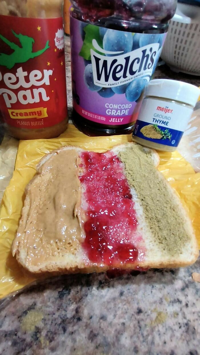 Peanut butter, grape jelly, and ground thyme spread side-by-side on a slice of bread in a cursed food picture.