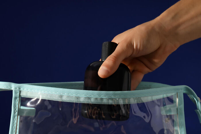 Hand placing a black travel bottle into a clear toiletry bag, demonstrating golden travel hacks for packing efficiently.