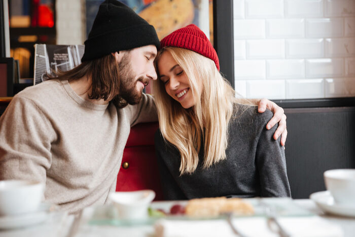Young couple wearing beanies shares a tender moment in a cafe, reflecting signs of a challenging childhood experience.