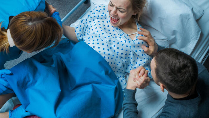 A woman in labor in a hospital bed supported by medical staff and a partner during childbirth and postpartum care.