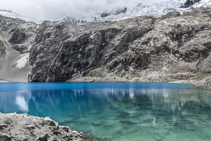 Turquoise mountain lake surrounded by rocky cliffs and snow, showcasing breathtaking travel photos from the community.