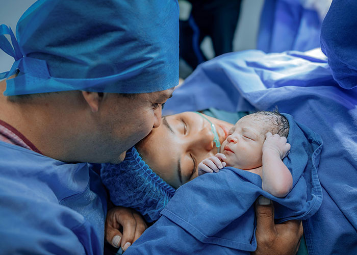 New dad holding newborn baby in birthing room, sharing first-time experience filled with emotion and joy.
