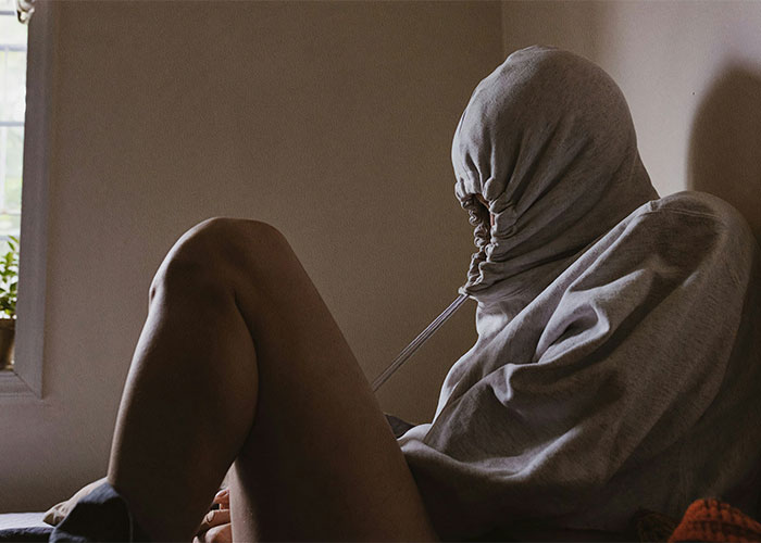 Person sitting indoors wearing a hoodie pulled tightly over their face illustrating creepy facts that might get stuck in your brain forever.