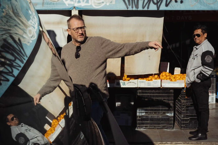 Man pointing while standing near fruit stall, captured in a candid street photo by Alex McClintock.