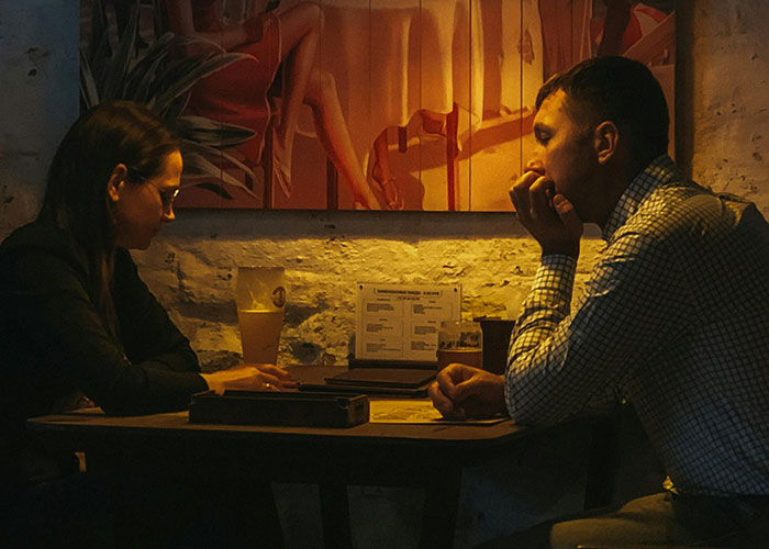 Couple sitting awkwardly at a dimly lit table with drinks, experiencing one of the most painful and awkward dates.