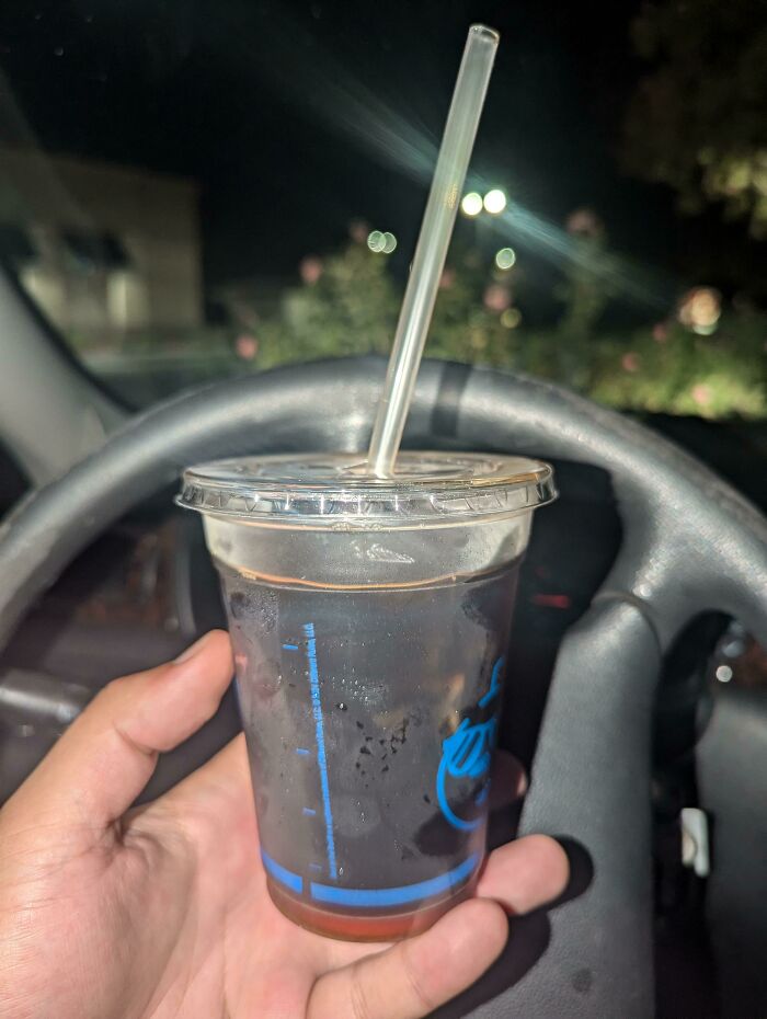 Hand holding a cold drink cup with a straw inside a car at night, illustrating a moment related to traumatizing the next generation.