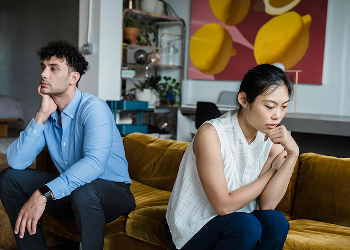 Couple sitting apart on couch looking upset, illustrating emotional impact of called off engagements and relationship struggles.