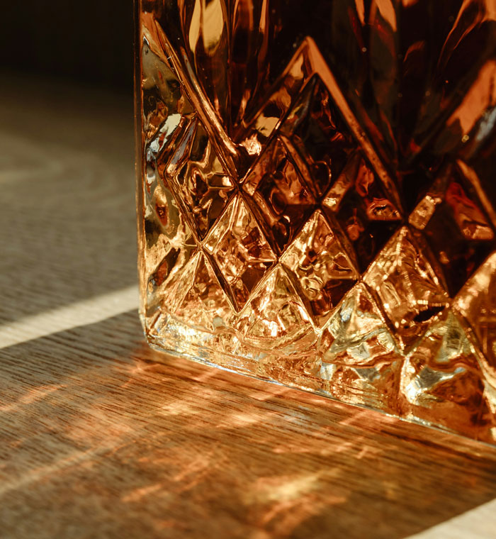 Close-up of textured amber glass casting patterns on a wooden surface, symbolizing reflection on biggest life mistakes.