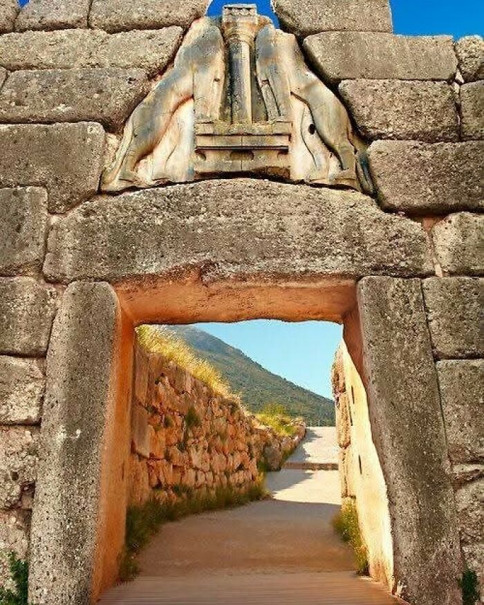 Ancient stone gateway with lion relief sculpture at an archaeological site under clear blue sky.