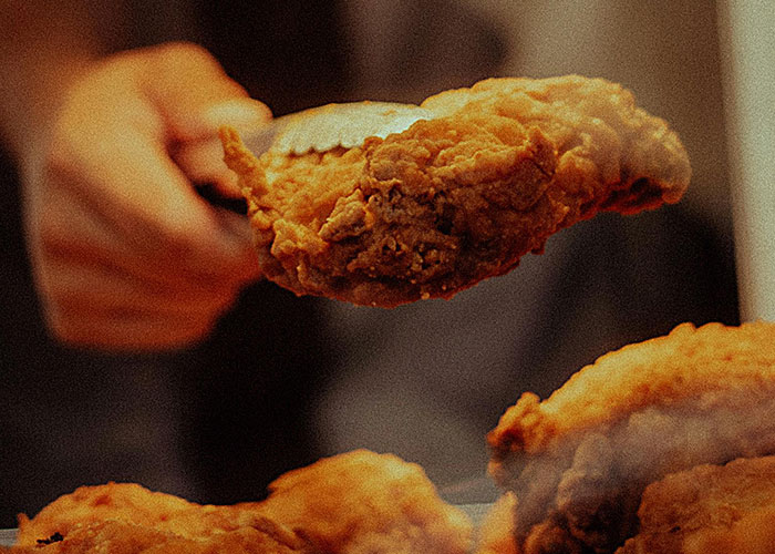 Close-up of a buffet worker serving crispy fried chicken with tongs, illustrating wildest encounters at buffets.