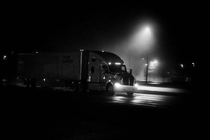 A semi-truck driving at night on a foggy road, capturing a creepy and scary moment from truck drivers lives.