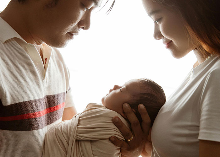 New father holding newborn baby with mother nearby, capturing the experience inside the birthing room for the first time.