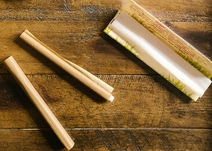 Two rolled cigarettes and an open rolling paper pack on a wooden surface showing take one for the team moment concept.