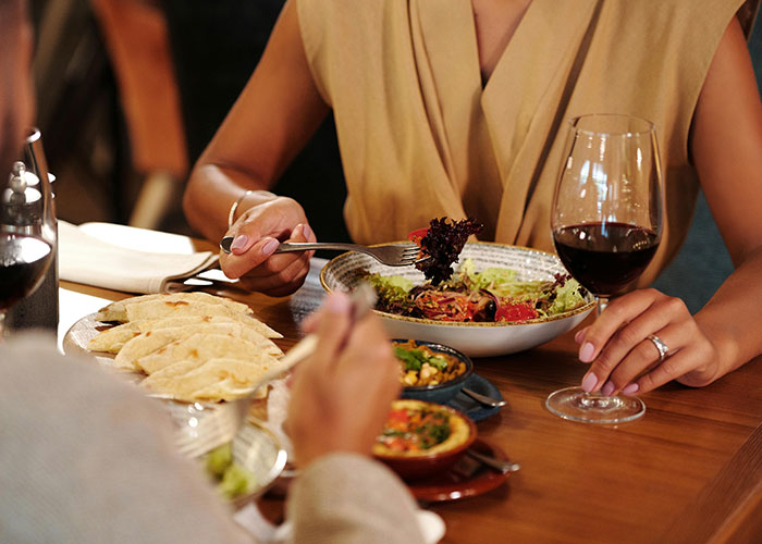 Couple having an awkward date at a restaurant with wine and salad, creating a painfully uncomfortable dining experience.