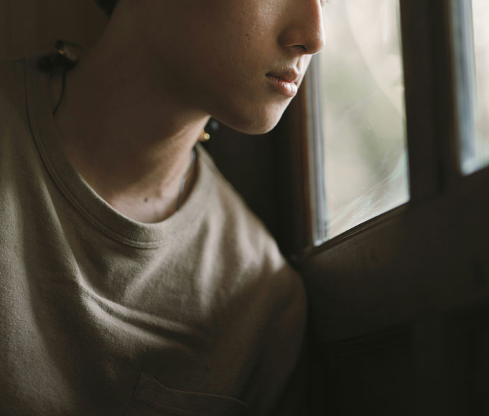 Young person looking thoughtfully out a window, reflecting on how they paid for college and financial secrets.