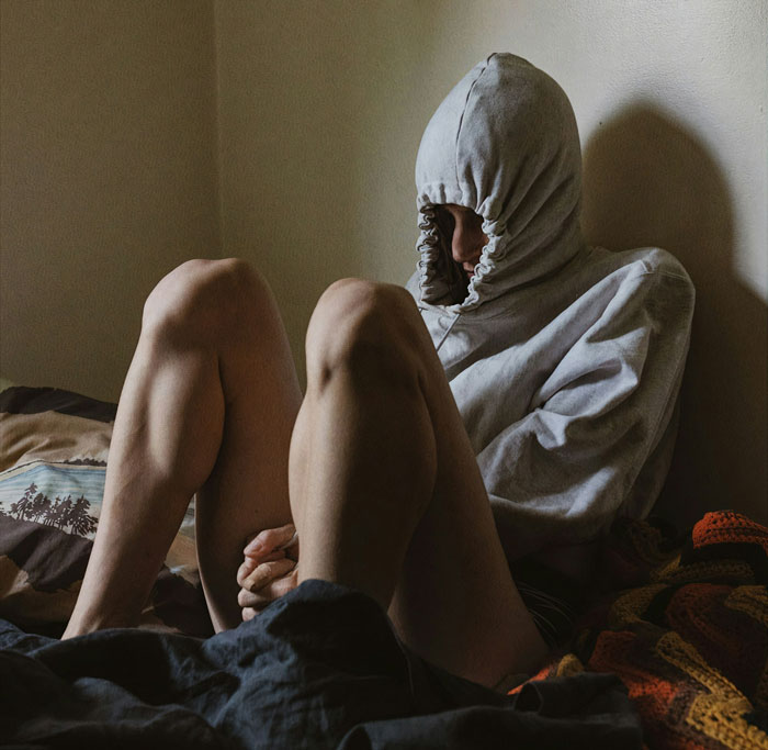 Person sitting on a bed with hood pulled tight, depicting intense emotions and profound revelations in therapy sessions.