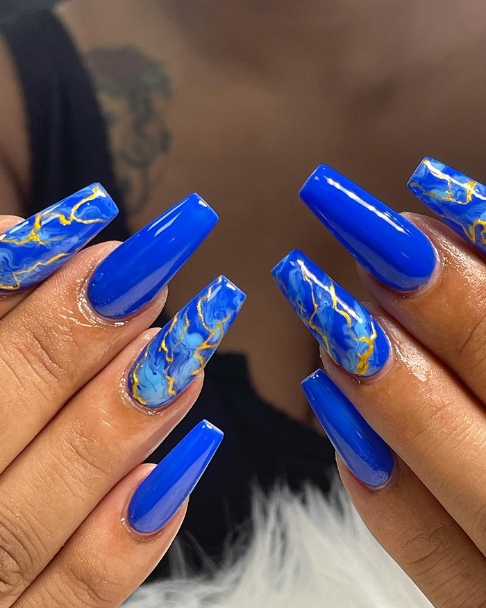 Bright blue summer nails with marble and gold swirl designs, showcasing a trendy and bold look for 2025’s hottest summer nails.