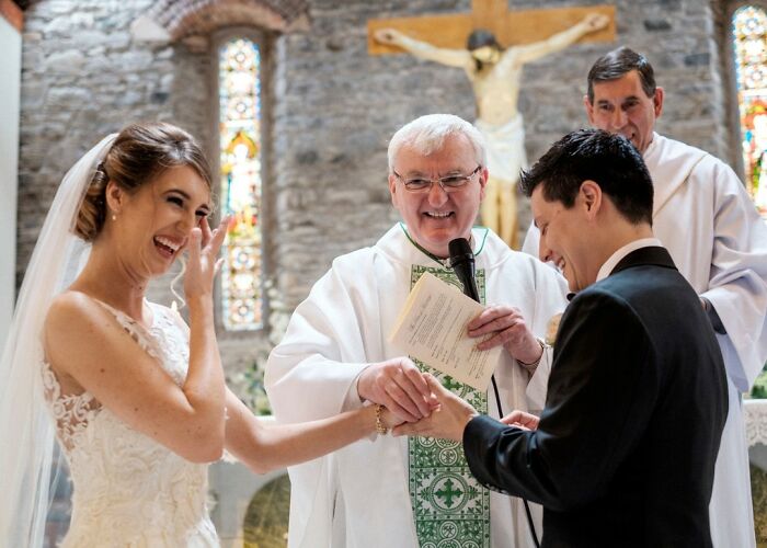 Bride and groom smiling during a wedding ceremony in church with priest exchanging rings in unforgettable wedding photos.