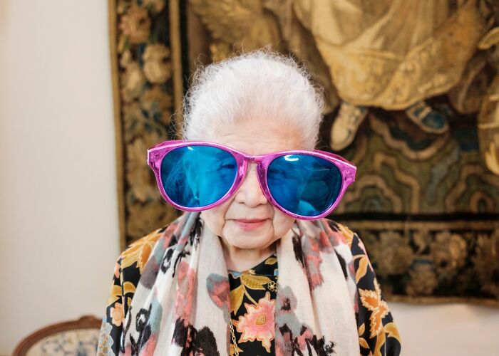 Elderly woman wearing oversized colorful sunglasses, posing playfully in a memorable wedding photo setting.