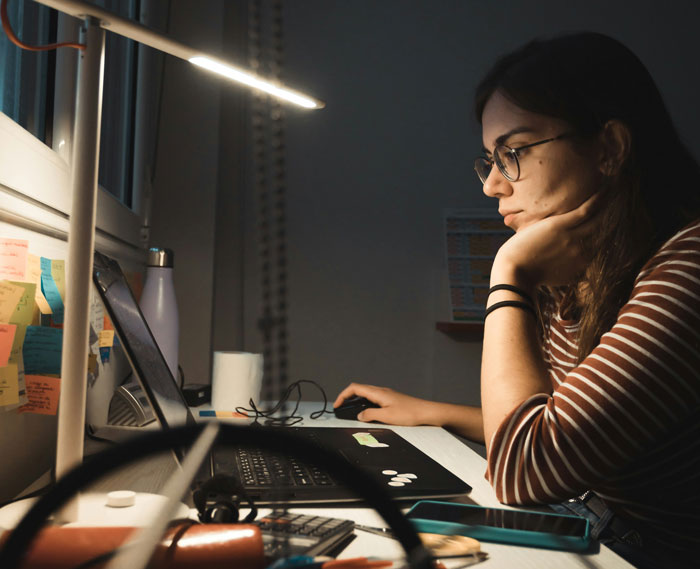Freelancer working late at home, focused on laptop, managing demanding client requests in a dimly lit workspace.